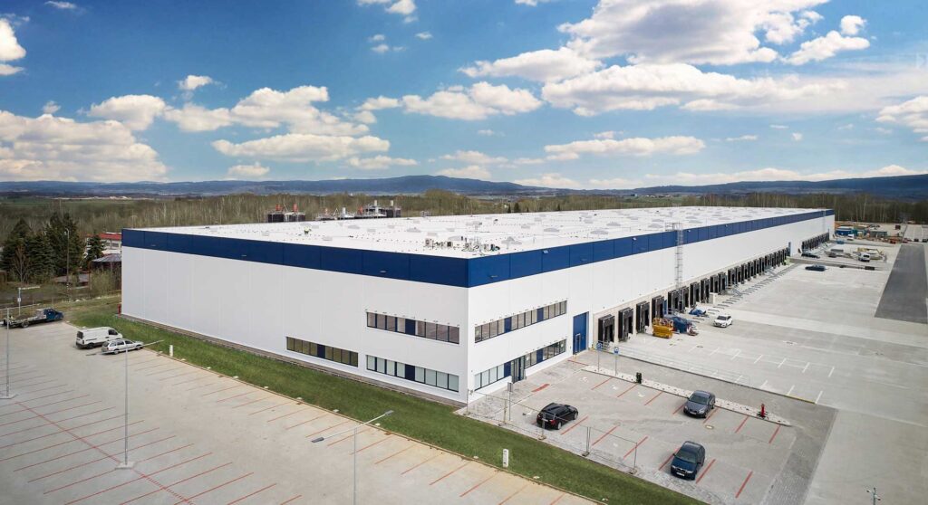 Hello friends! Imagine if you will, a pristine white building with charming blue trim nestled beneath a partly cloudy sky, like a scene straight out of your favorite feel-good movie. This isnt just any building—its ShipMonks state-of-the-art warehouse facility. Specializing in Third Party Logistics, its more than just an operational center; it’s where efficiency meets innovation. Surrounded by a parking lot bustling with eager vehicles, this setting is nothing short of picturesque. The distant trees and gently rolling hills paint the perfect backdrop for what could easily be described as an inspiring snapshot of modern commerce. While were often caught up in the hustle and bustle of daily life, places like this remind us that even logistics has its own beauty—a harmony between man-made precision and natural elegance. ShipMonk.com isnt just about moving boxes; its about moving dreams forward with grace and reliability. Now thats something worth celebrating!. via ShipMonk.com